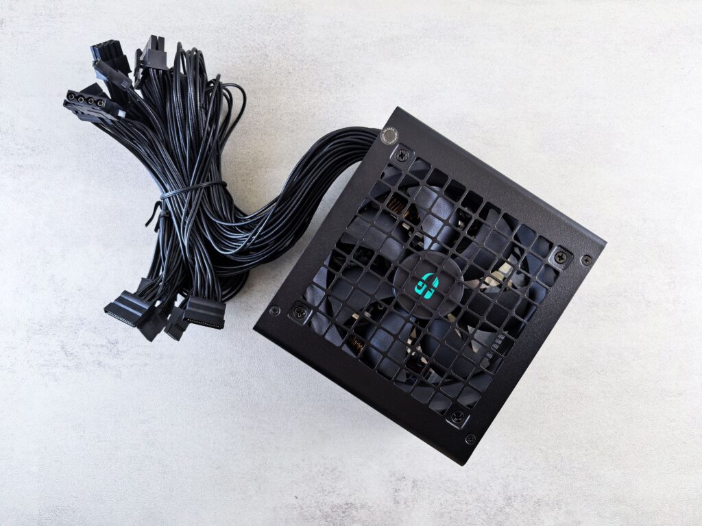 Black ATX power supply with its cables bundled beside it on a grey surface